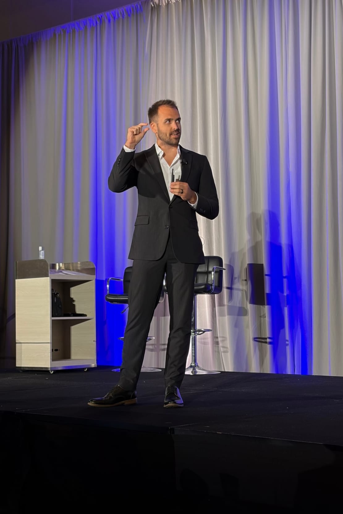 Nick Fischer speaking on a stage lit in blue at a chiropractic seminar.